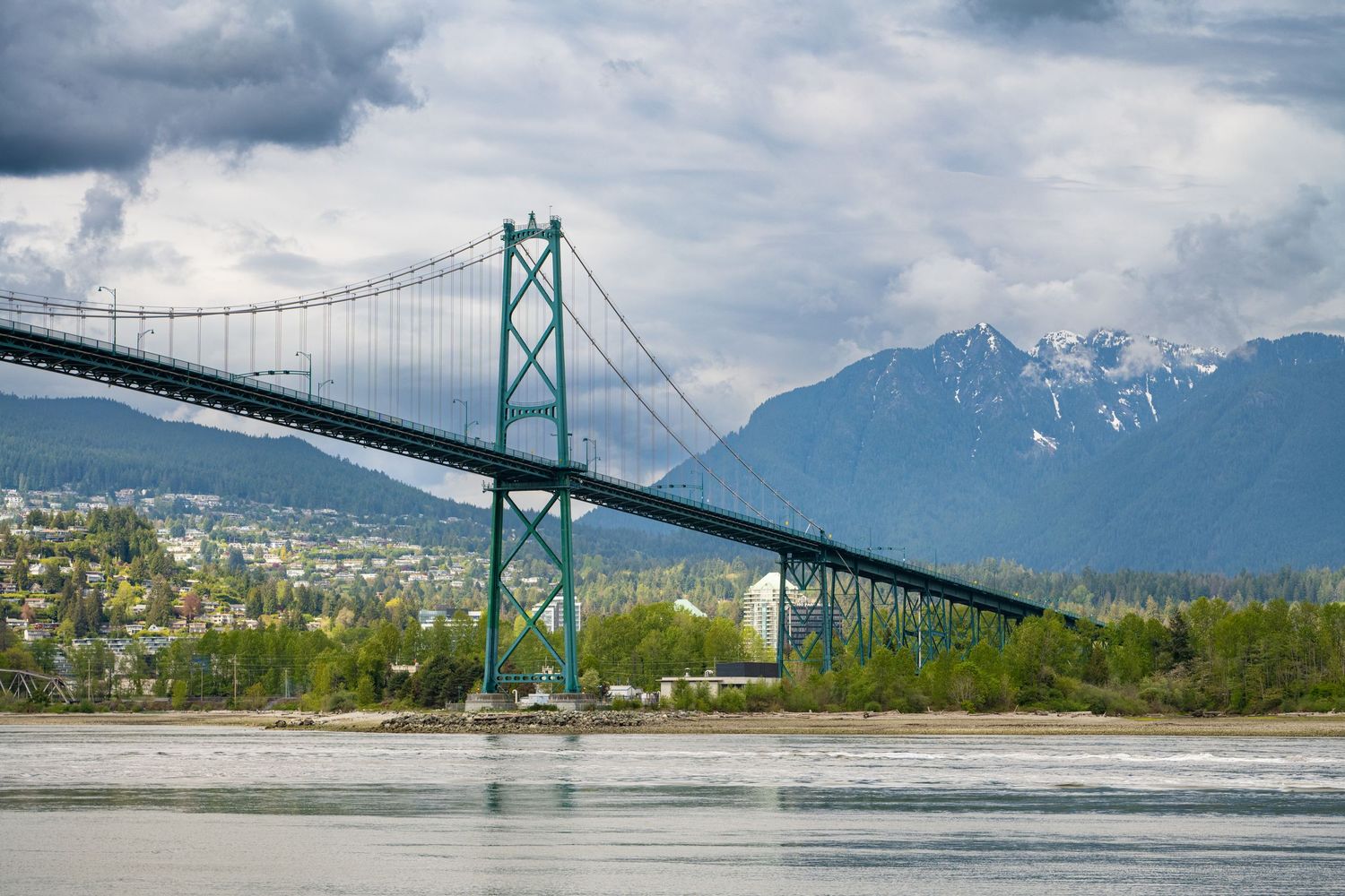 Lions Gate Bridge spans across Vancouver harbor with snow-capped mountains visible in the misty background.