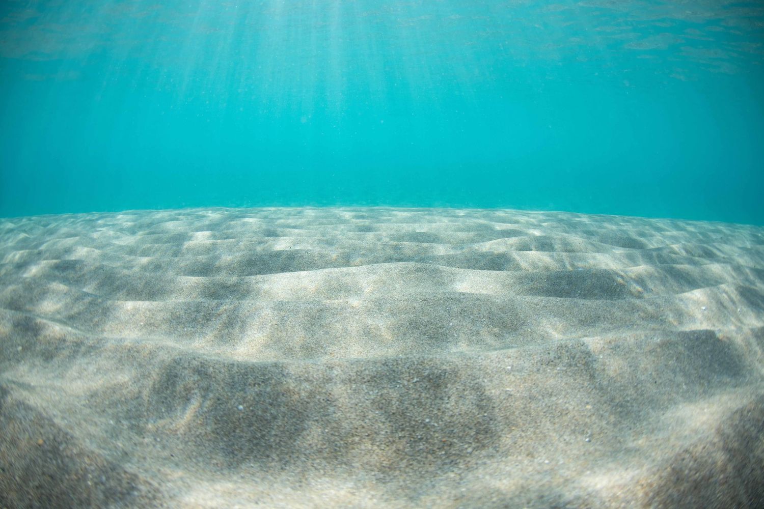 Sunbeams penetrating crystal clear turquoise waters over sandy ocean floor.