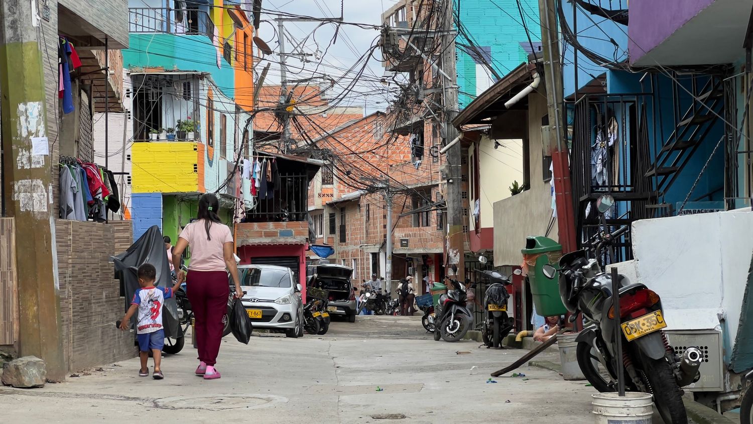 Narrow street with colorful buildings and hanging power lines in a dense urban neighborhood of Medellin, Colombia.