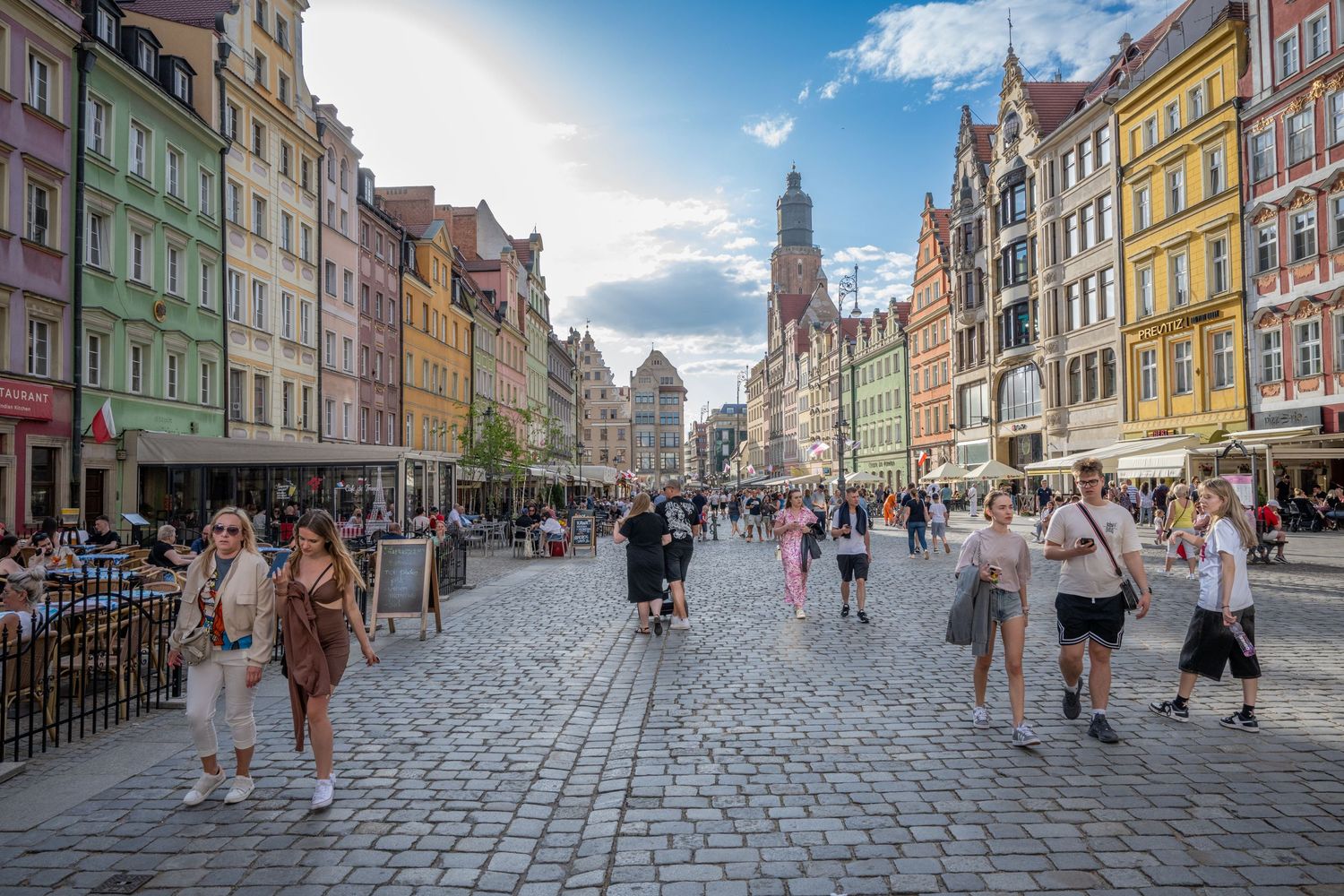 Colorful historic buildings line a cobblestone street in Wroclaw's Market Square as tourists explore the pedestrian area.