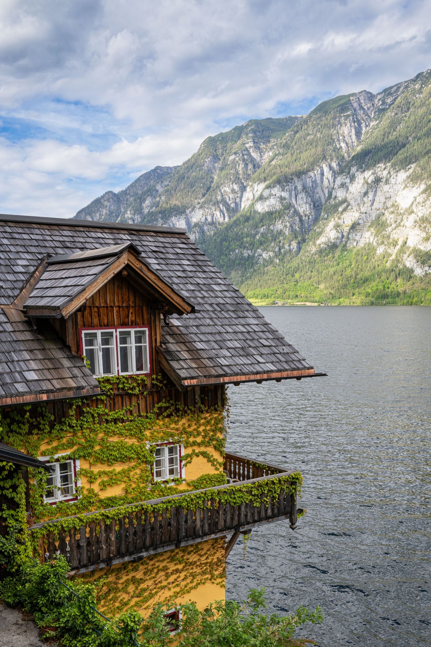 A rustic wooden cabin with a green roof perched on the shore of a mountain lake in Hallstatt, Austria.