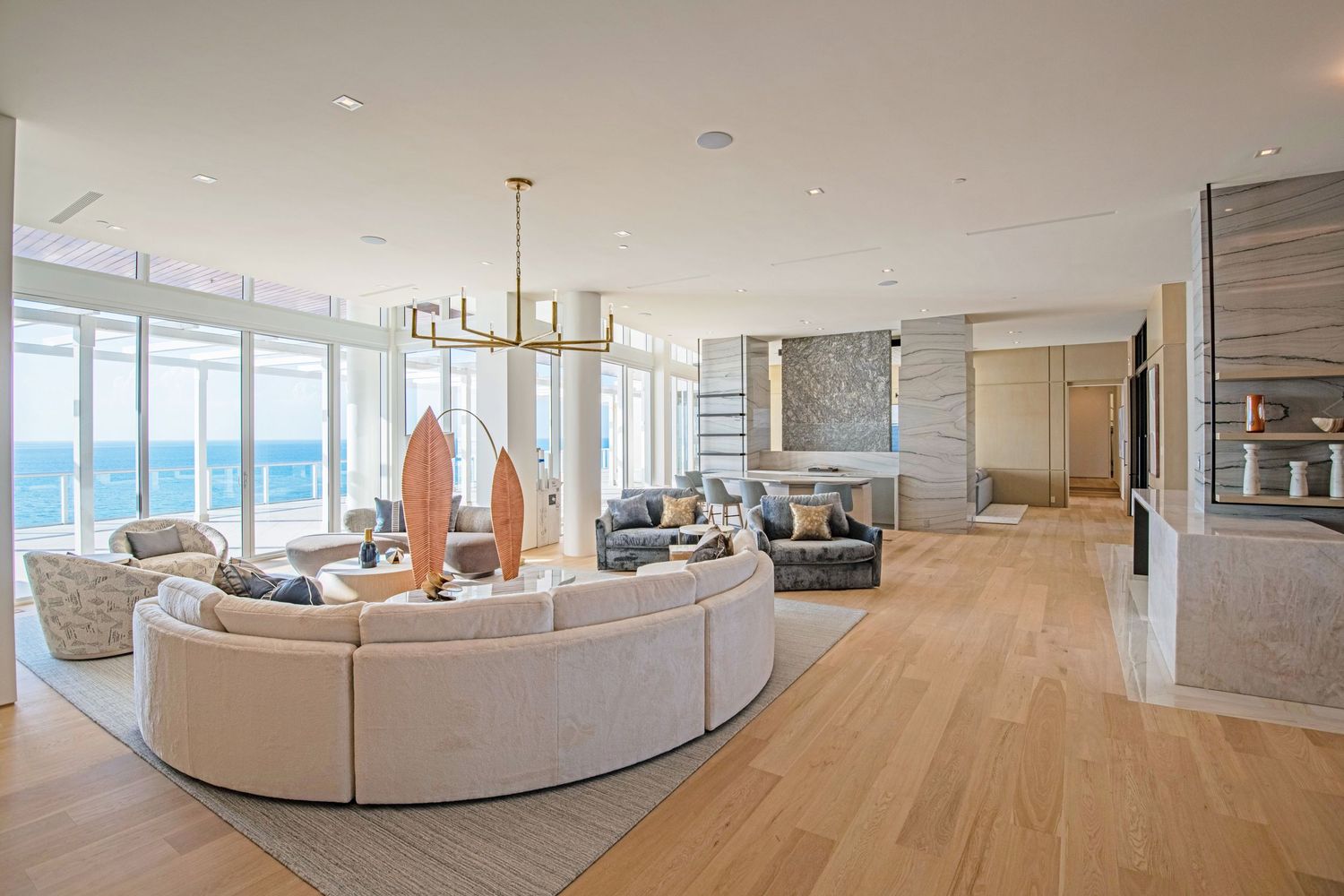 Modern luxury oceanfront condo with curved white sectional sofa, light wood floors and floor-to-ceiling windows.