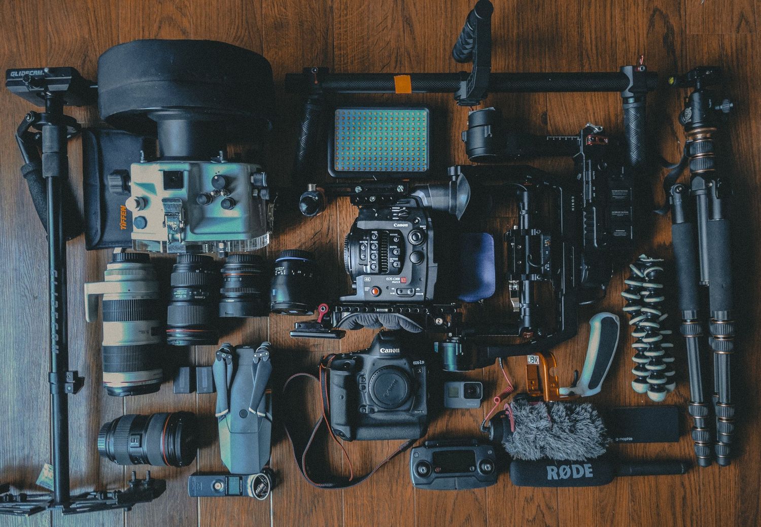 Professional camera equipment and lenses arranged on a wooden surface in a dark moody setting.