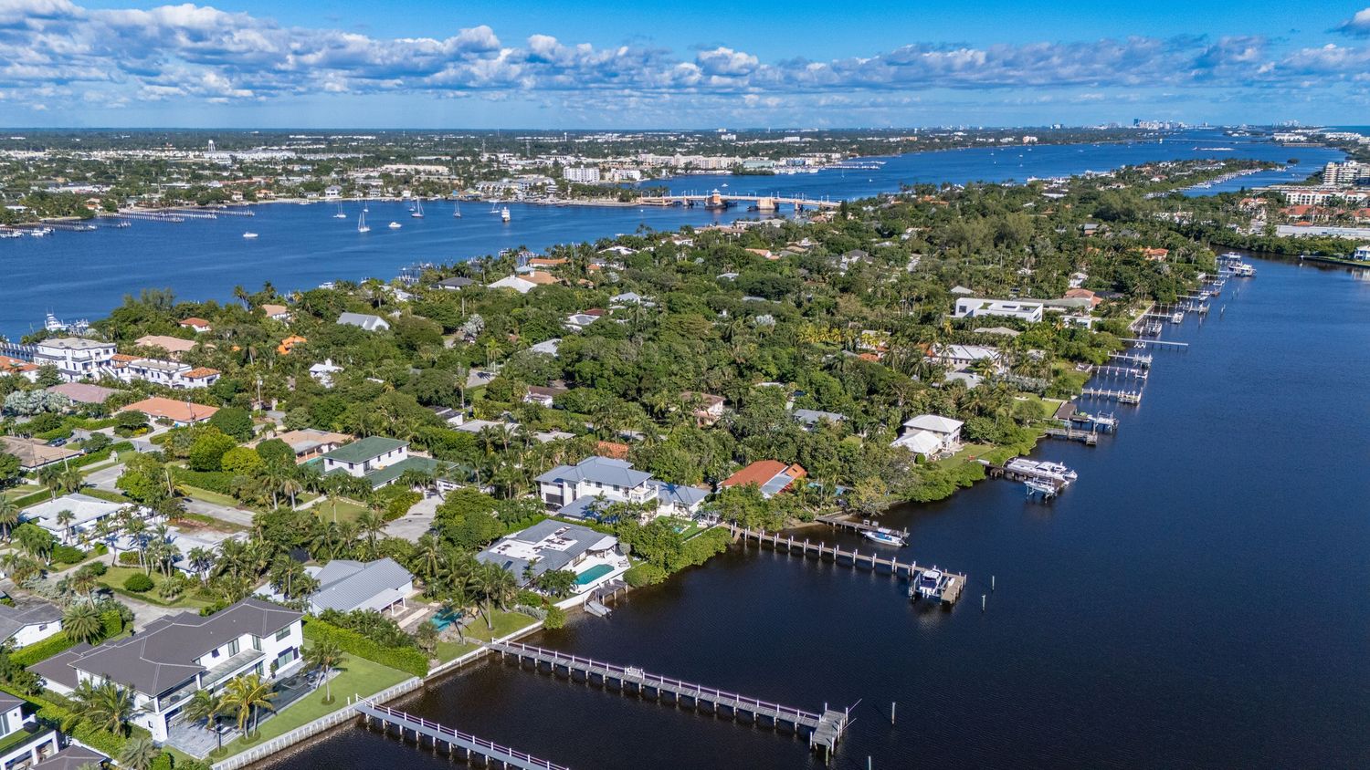 Aerial panoramic view of coastal waterfront homes and docks along Florida's intracoastal waterway on a sunny day.