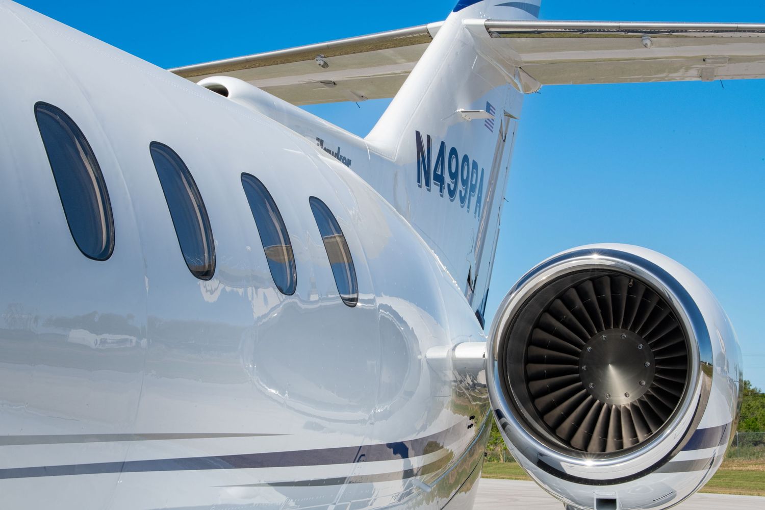 Close-up details of a sleek private jet showing its engine, fuselage and windows against a bright blue sky.