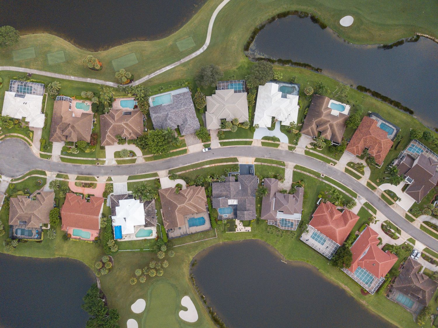 Aerial view of residential houses with red roofs surrounding a small lake in a suburban neighborhood.