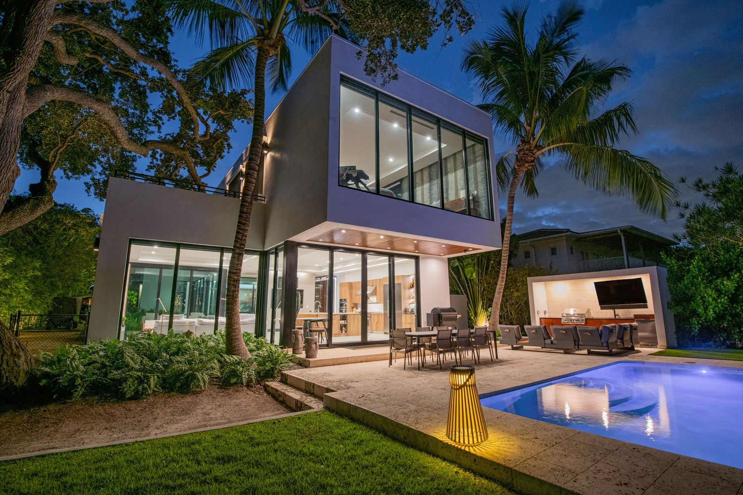 Modern luxury villa with illuminated pool and palm trees at dusk showcases sleek architectural design and landscaping.