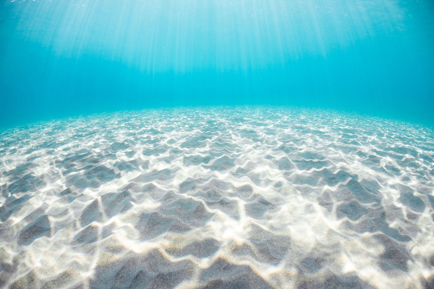 Underwater sunbeams creating light patterns on sandy ocean floor through crystal clear water.