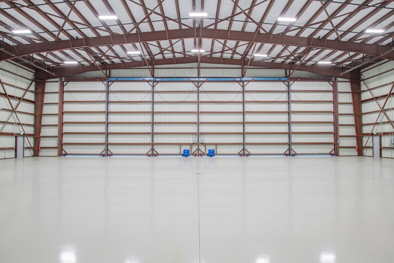 Interior view of a large empty warehouse facility with exposed metal beams and white walls.