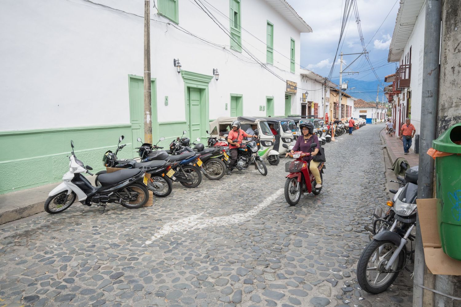Motorcycles parked along a cobblestone street with white and green buildings in a historic Latin American town.