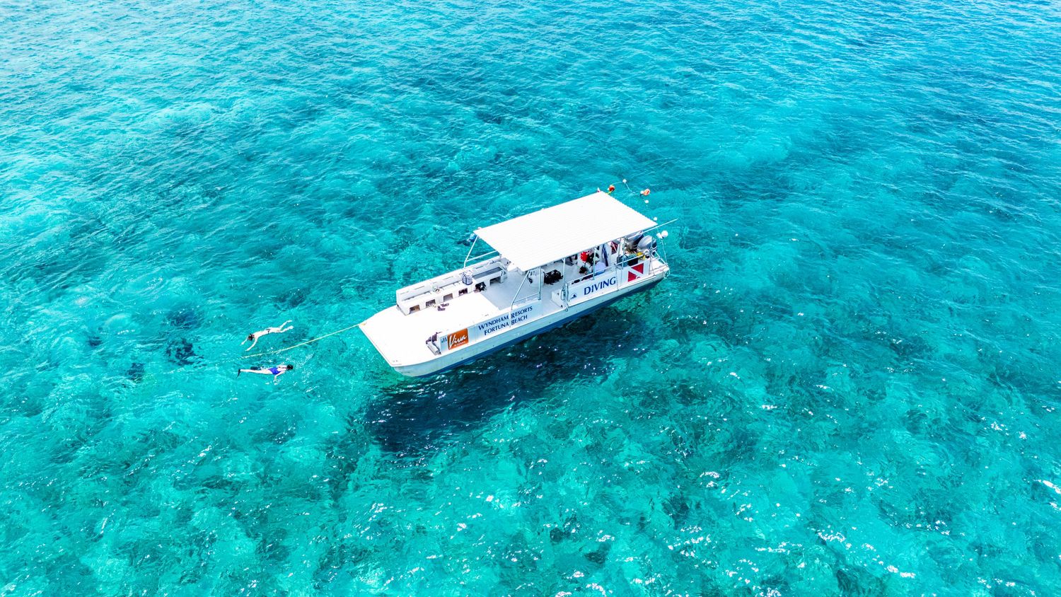 Aerial view of boats cruising through crystal clear turquoise waters near a tropical reef in the Caribbean Sea.