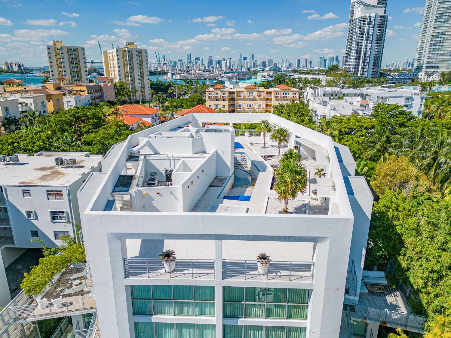 Aerial view of a modern white penthouse rooftop terrace with Miami skyline and Biscayne Bay in the background.