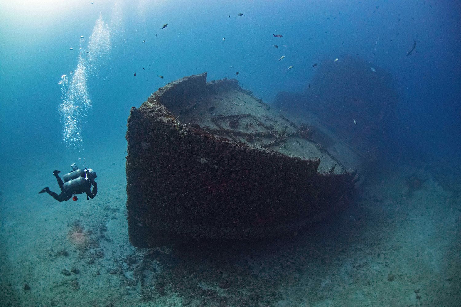 Underwater shipwreck resting on ocean floor with sunbeams filtering through blue waters.