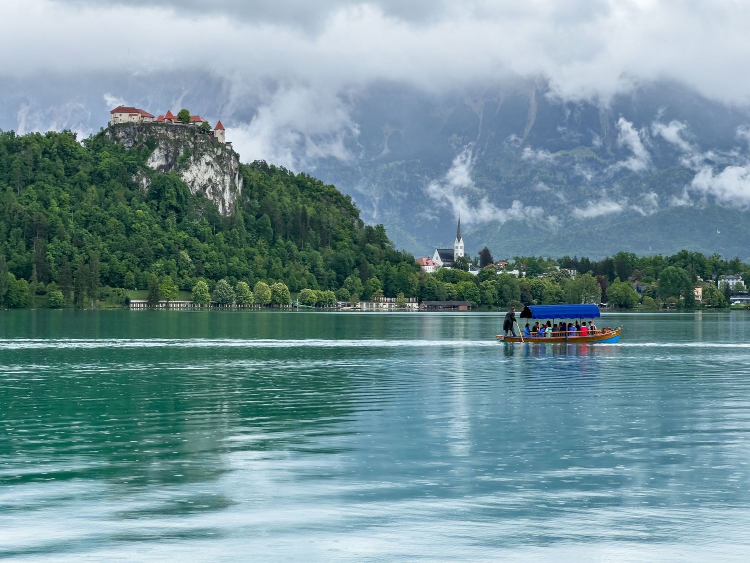 A panoramic view of Lake Bled in Slovenia with its iconic island church and castle surrounded by misty mountains.