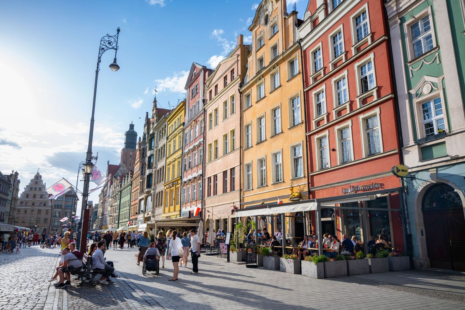 Colorful historic buildings line a bustling cobblestone street in Wroclaw's Market Square on a sunny day.