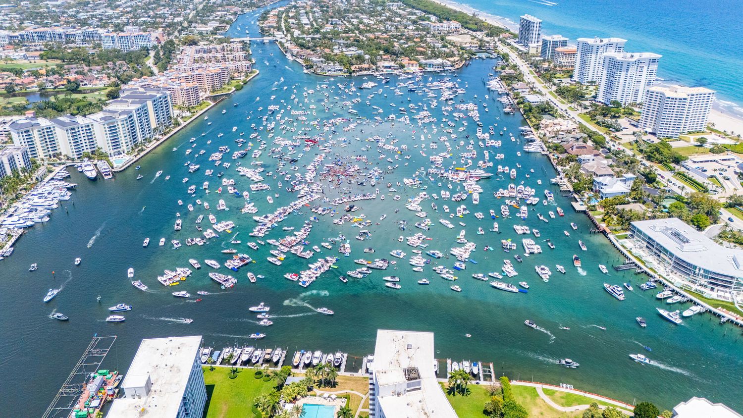 Aerial view of boats crowded in Boca Raton Inlet during a holiday weekend with condos and ocean in background.