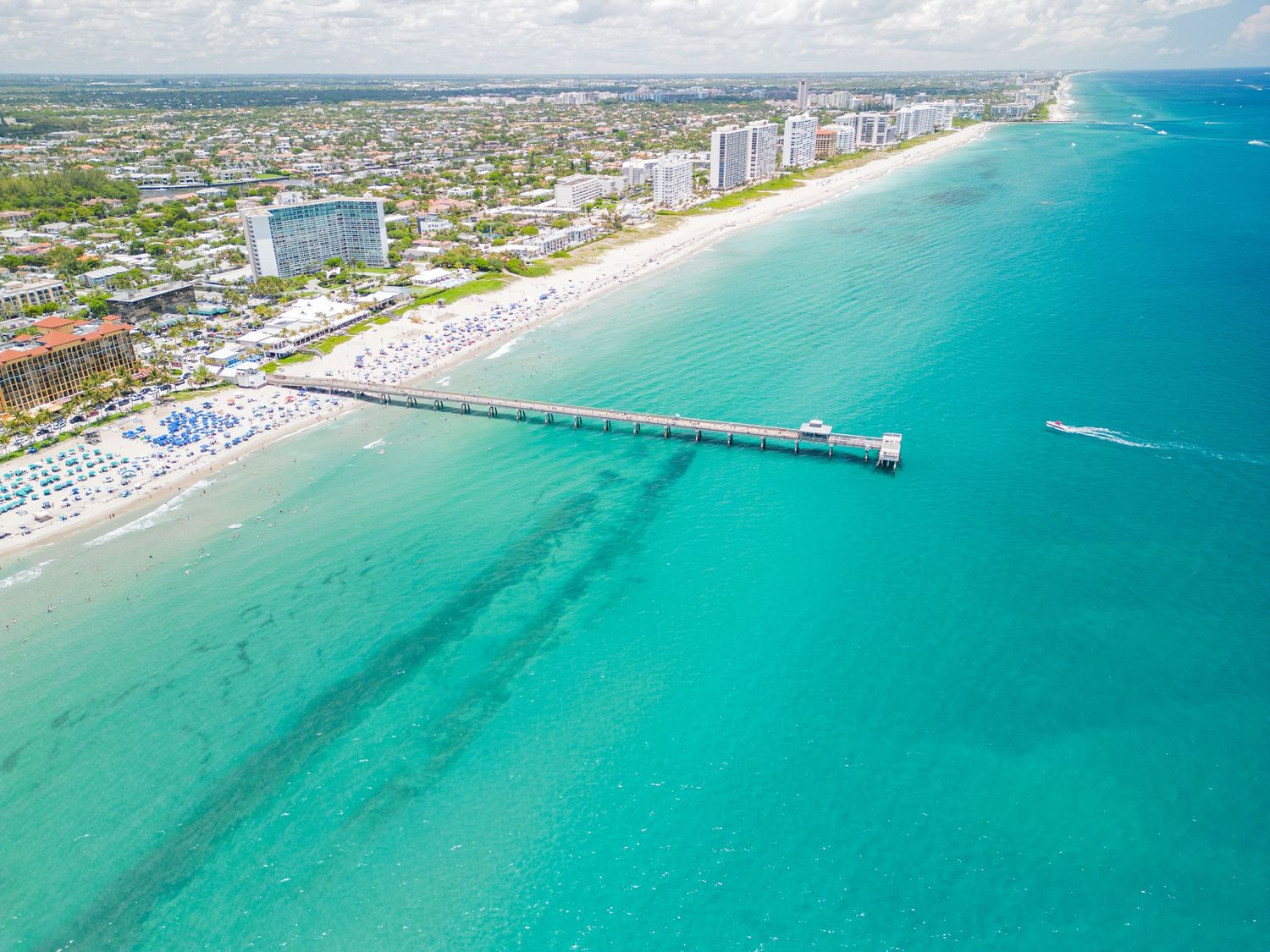 Aerial panoramic view of turquoise ocean waters and sandy beaches along a coastal city shoreline with high-rise buildings.