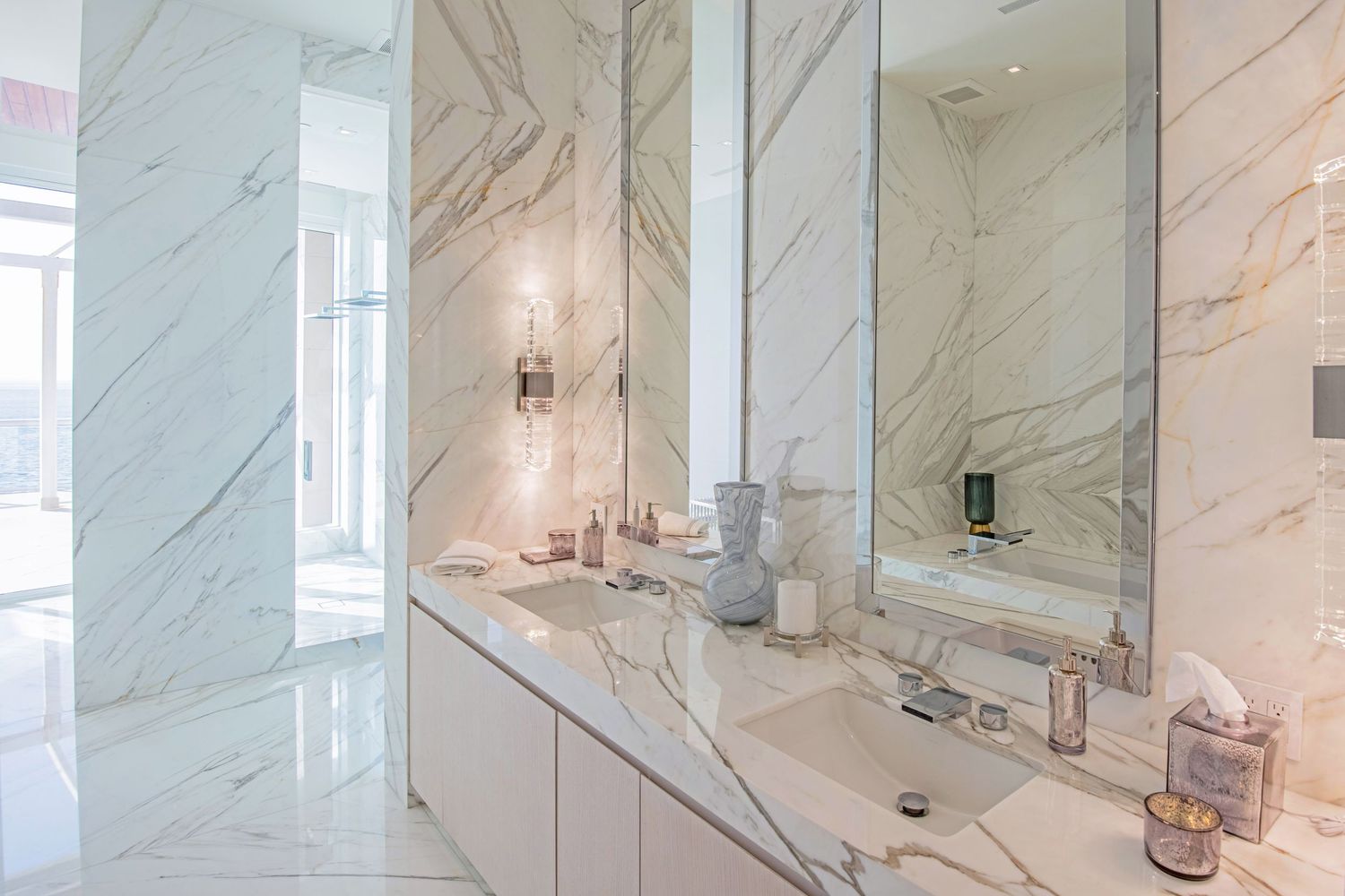 Luxurious marble bathroom interior with white walls, modern fixtures, and natural light streaming through tall windows.