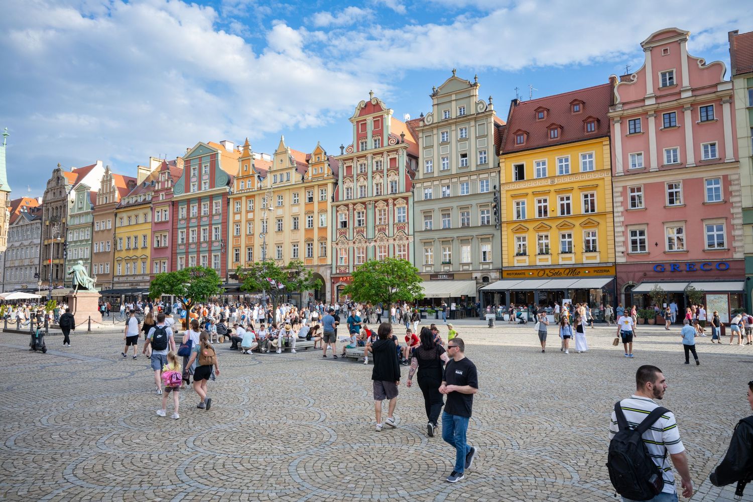 Colorful historic townhouses line the Market Square in Wroclaw, Poland as tourists explore the cobblestone plaza.