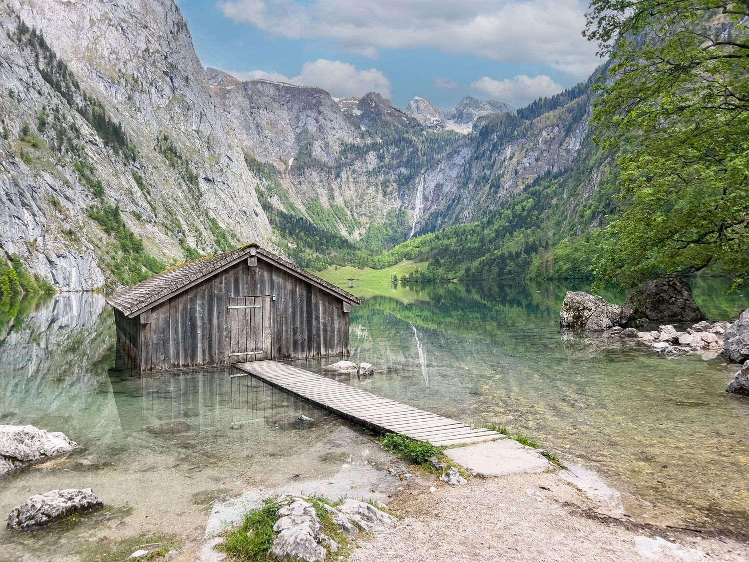 A scenic hiking trail winds along the edge of a crystal clear alpine lake surrounded by towering mountain peaks.