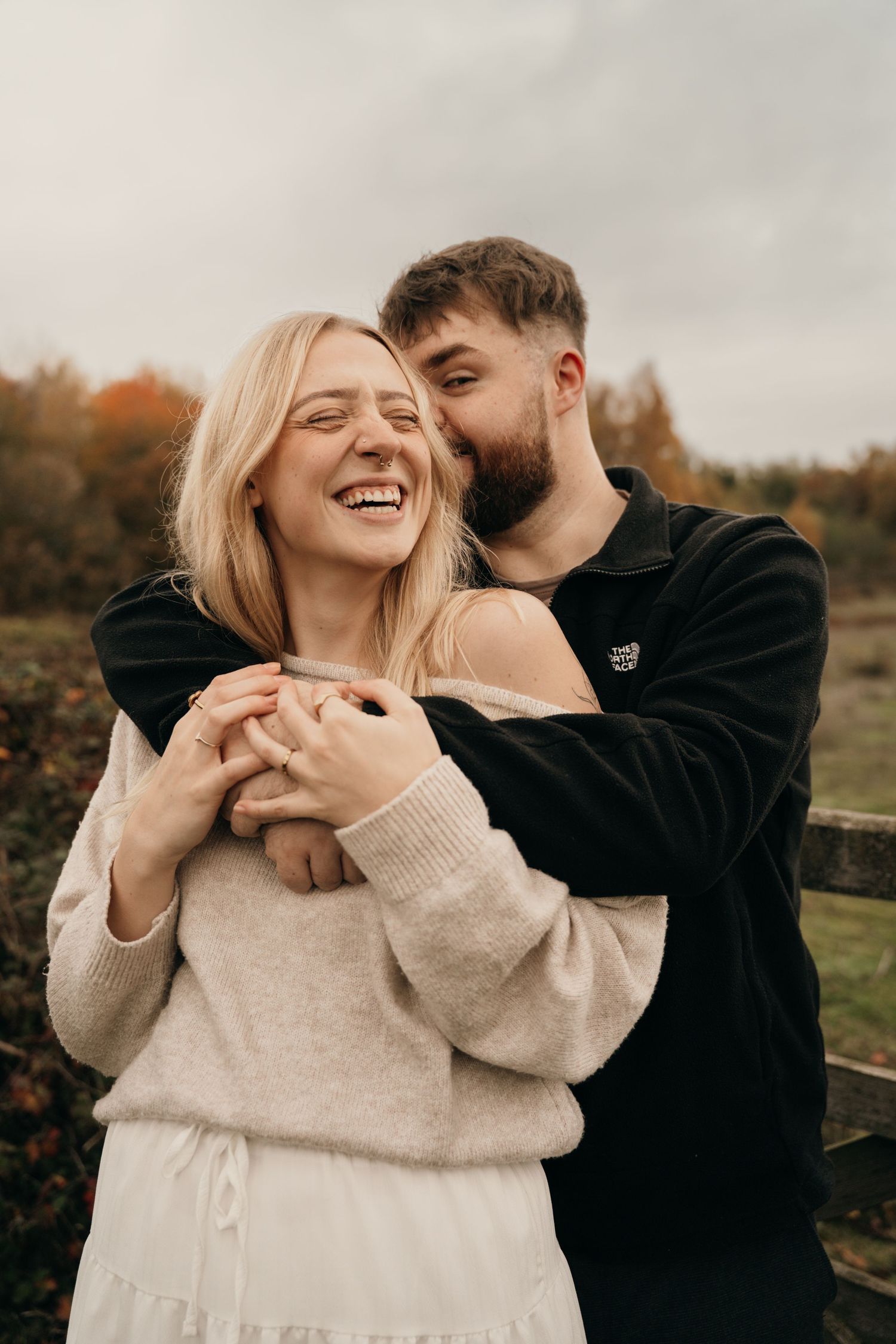 Man embracing laughing woman from behind outdoors in autumn, couple sharing joyful romantic moment.