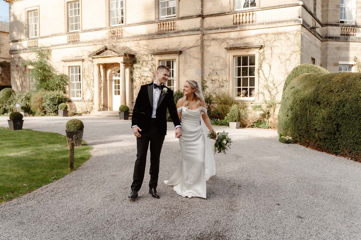 Bride and groom holding hands and walking in front of a beautiful stone country house venue.