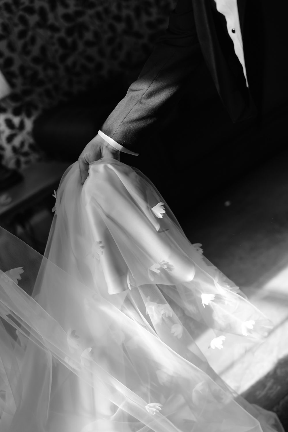 Close-up black and white shot of groom holding brides floral embroidered wedding veil.