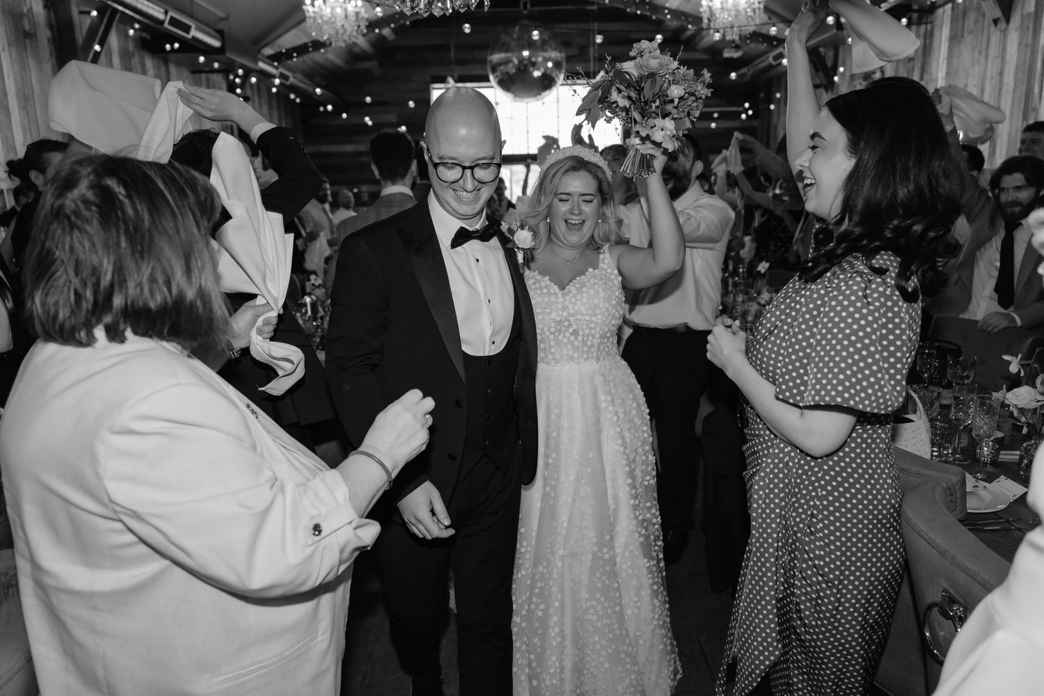Black and white photo of a bride and groom walking through guests at their wedding reception celebration.