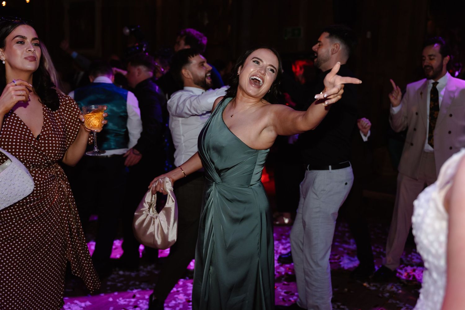 Woman in green dress dancing energetically at a wedding reception with guests on a purple-lit dance floor.