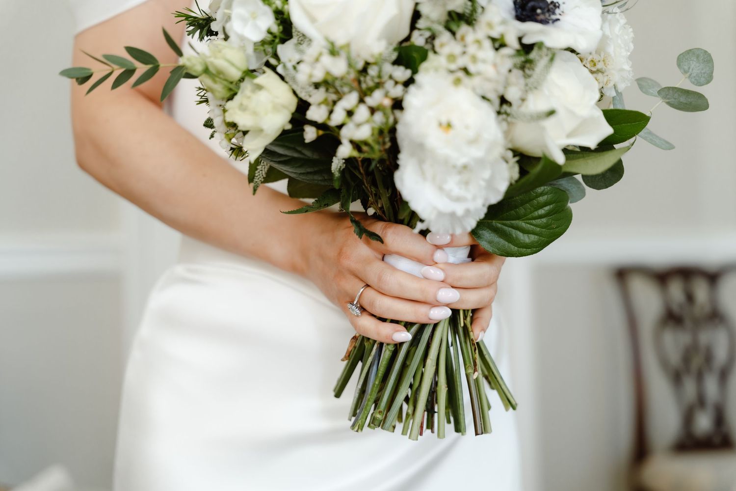 Bride in white satin gown holding elegant white and green wedding bouquet.