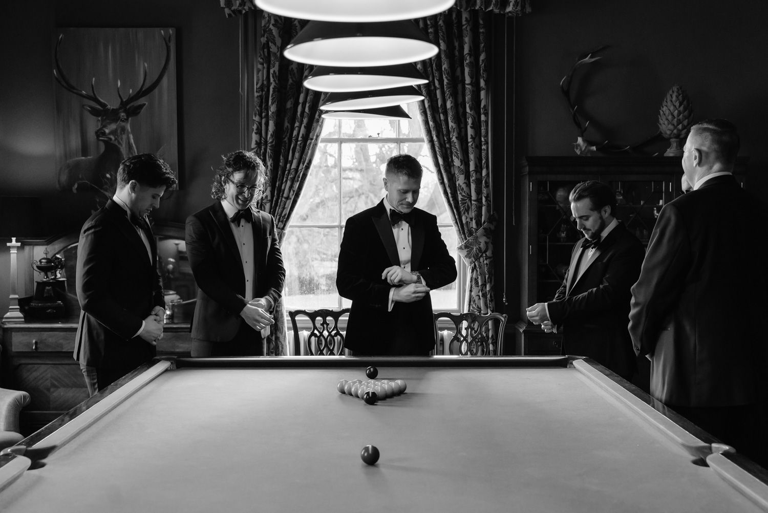 Black and white photo of groomsmen gathered around a pool table before wedding.