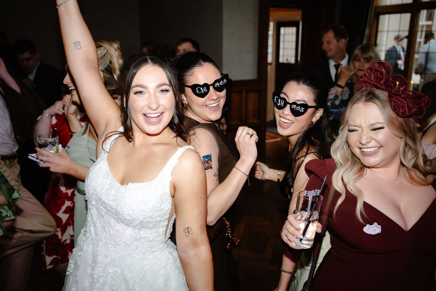 Bride in white dress celebrates with friends in sunglasses at a lively wedding reception party.