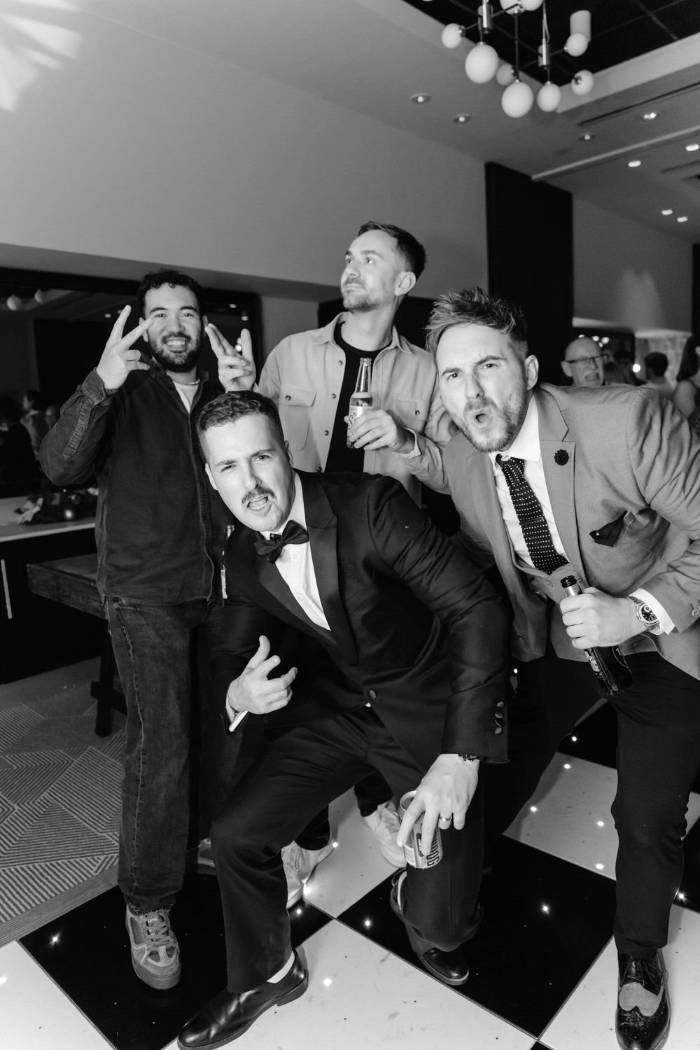 Black and white photo of groom and groomsmen posing playfully on dance floor.