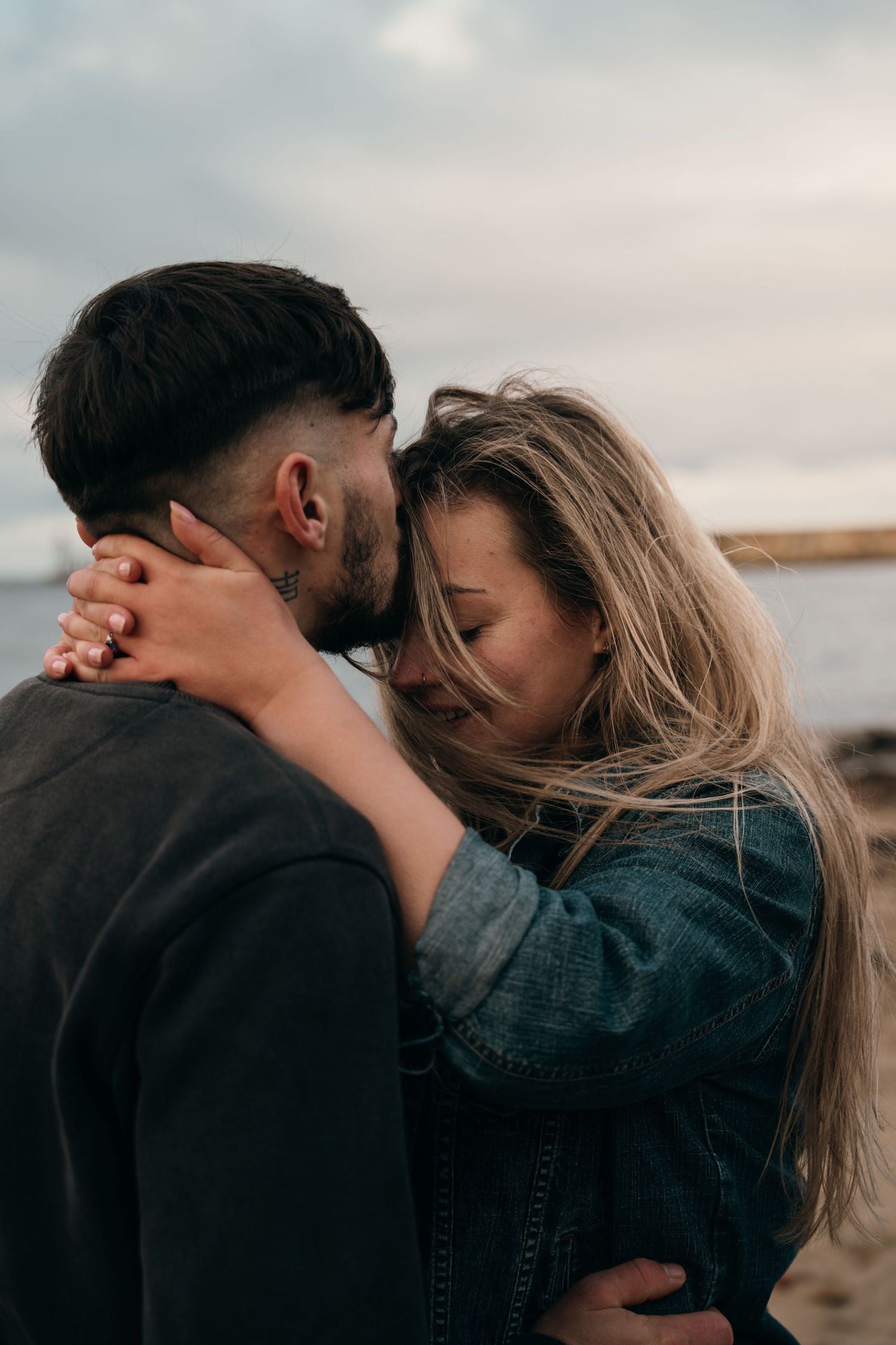 Loving couple embracing tenderly on a beach under a cloudy sky.