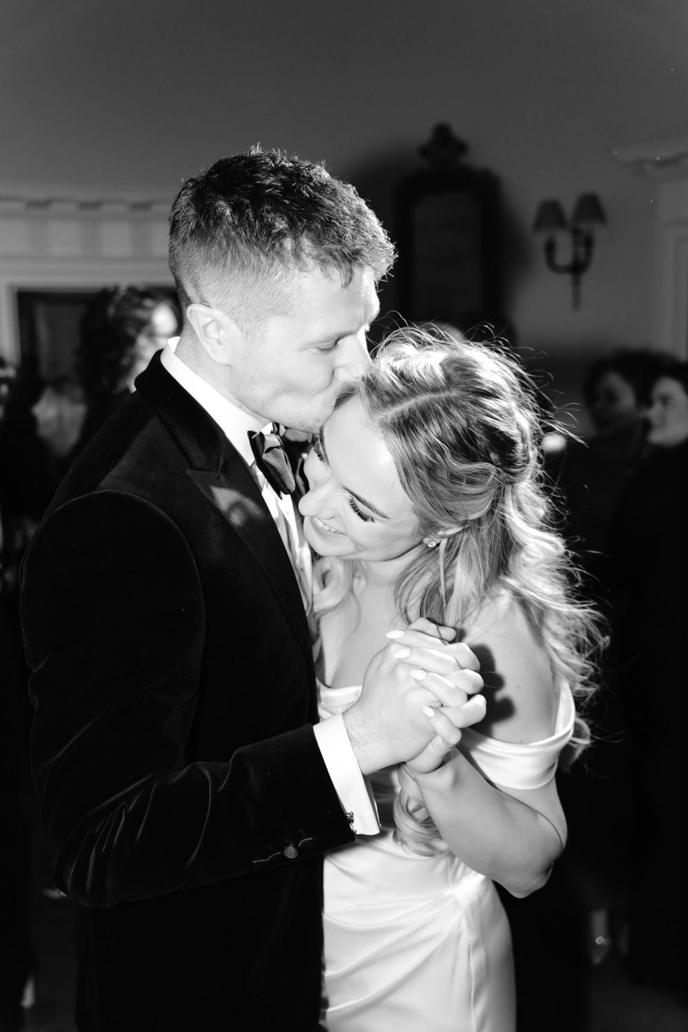 Black and white photo of newlyweds sharing their first dance, groom kissing bride on forehead.
