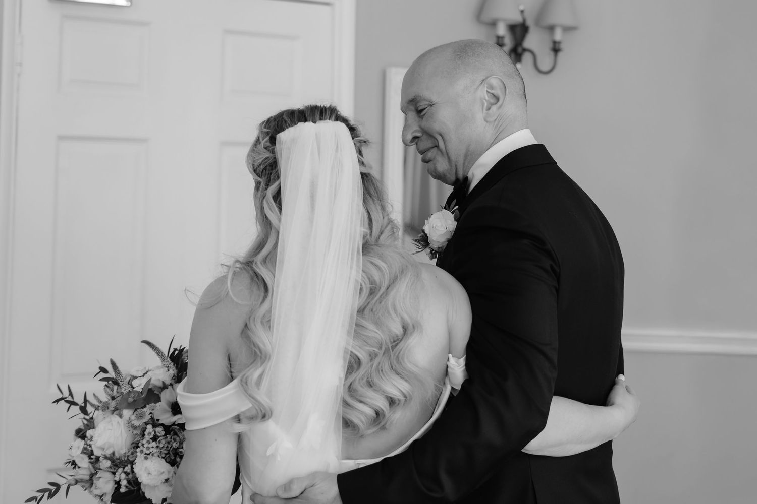 Black and white photo of bride sharing emotional first look moment with father.