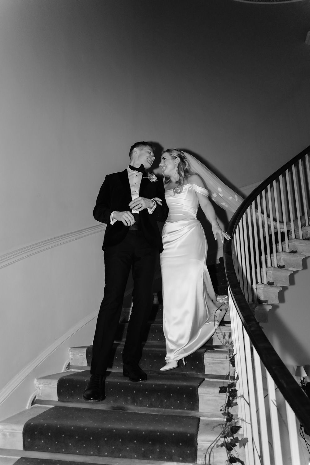 Bride and groom sharing a kiss on a curved staircase in black and white.