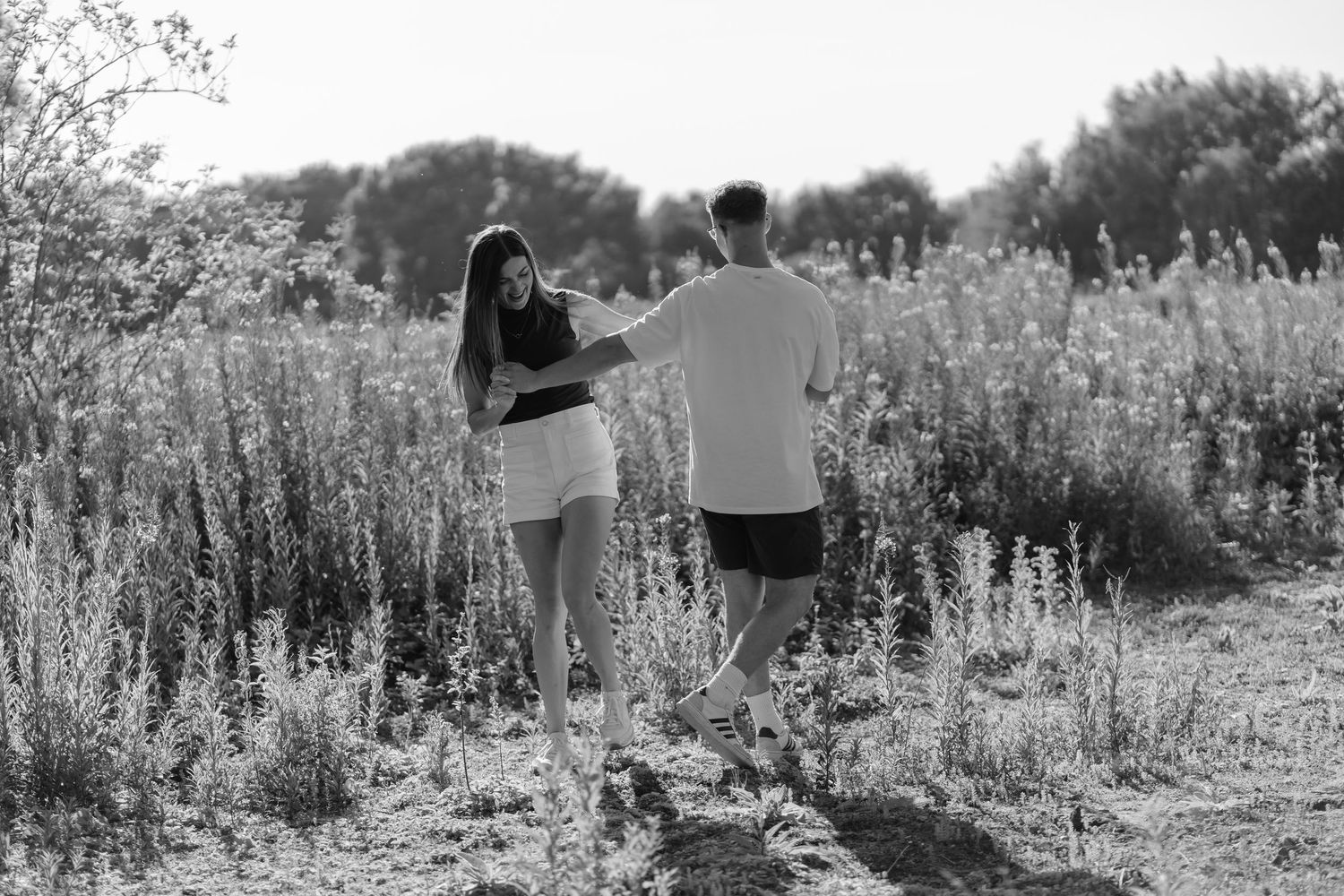 Black and white photo of a couple walking hand in hand through a wildflower field on a sunny day.