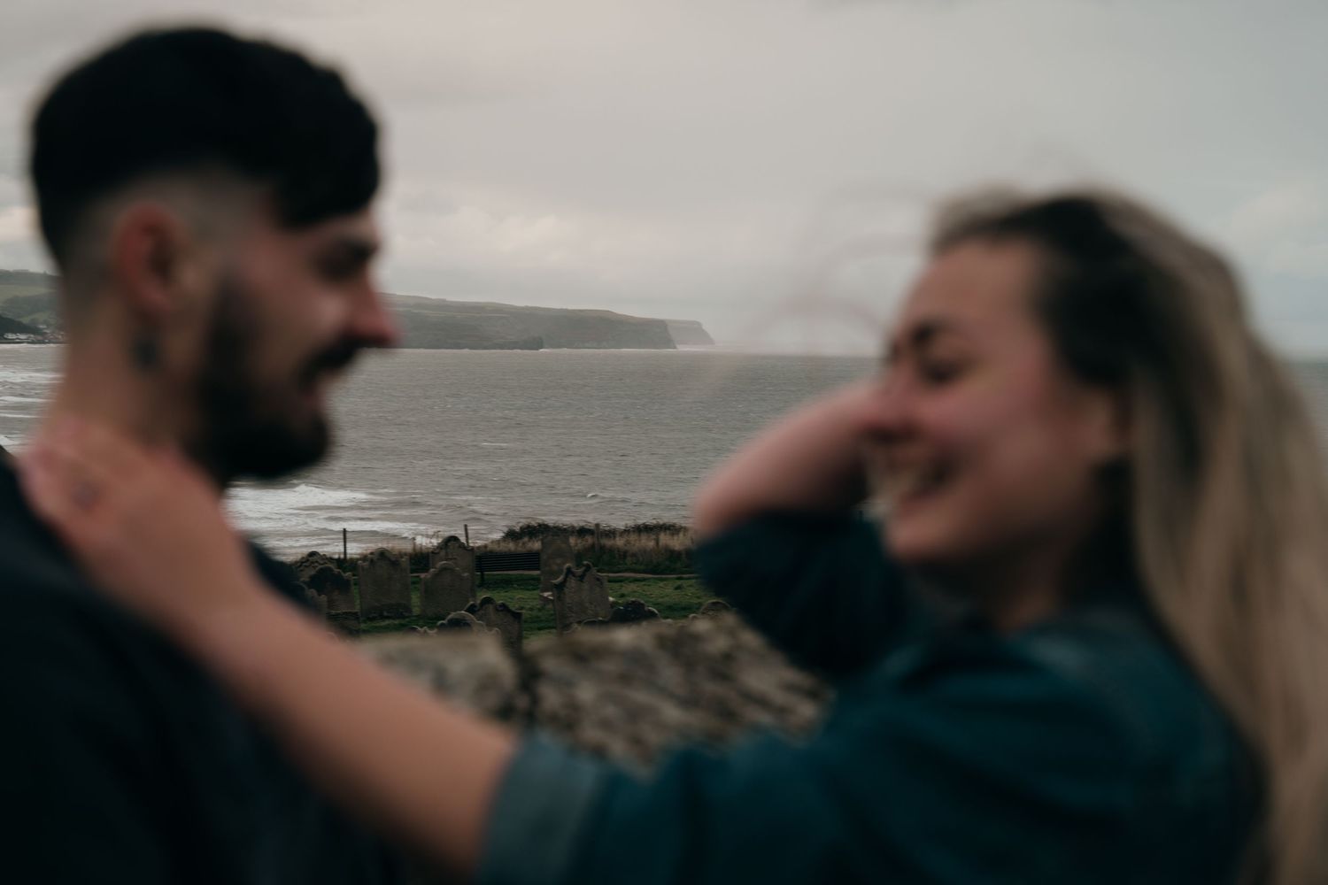 Couple sharing a joyful moment outdoors with scenic coastal cliffs and ocean in the background.