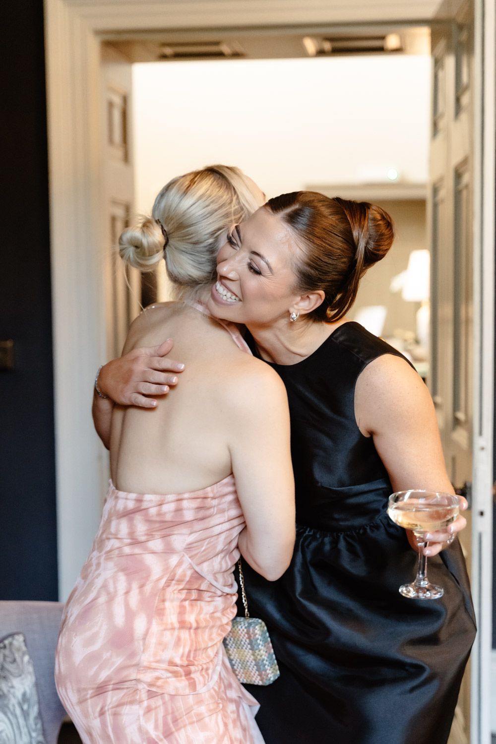 Two women sharing a warm embrace at a wedding celebration, one holding a champagne glass.