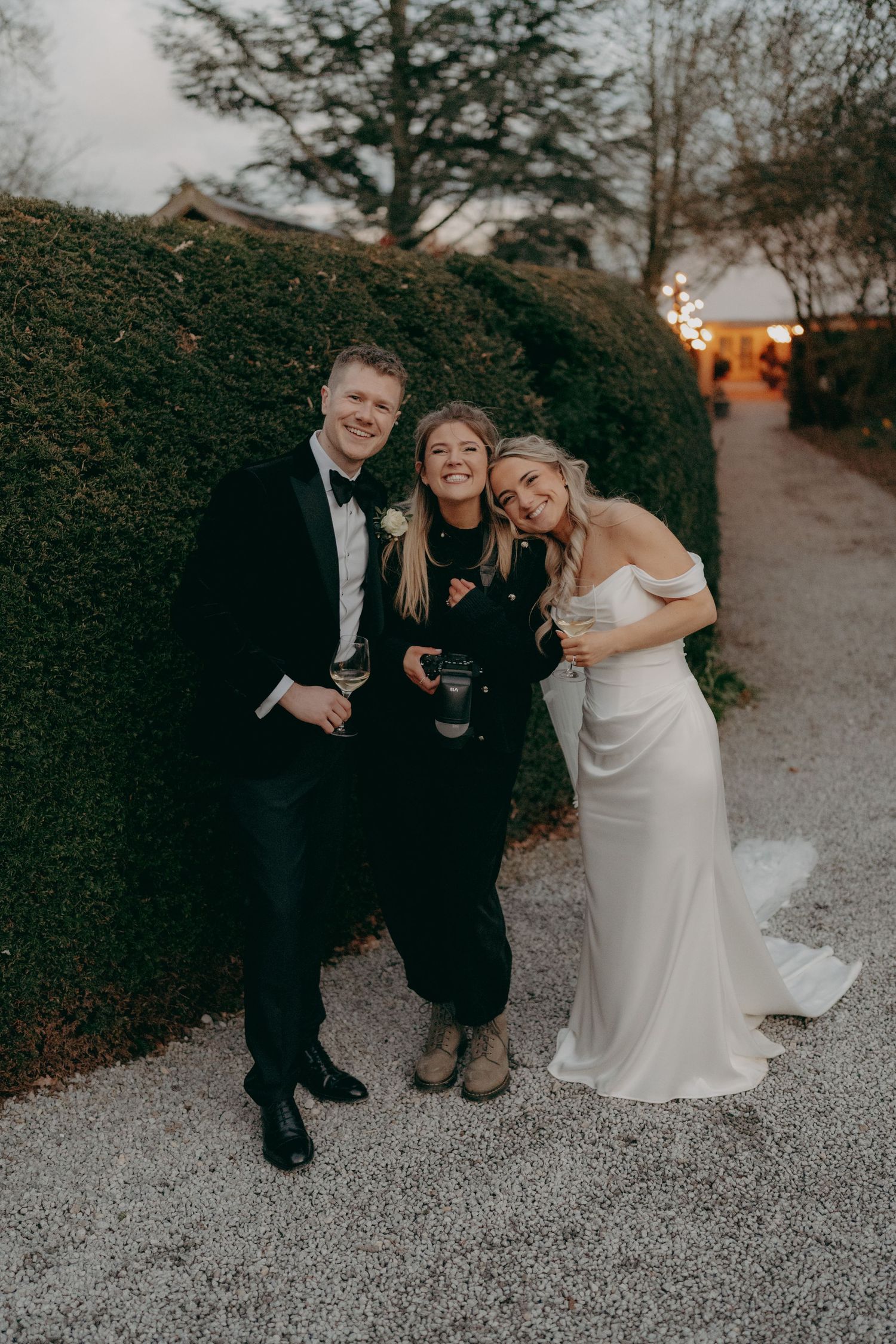 Bride and groom posing with wedding photographer outside venue at dusk.