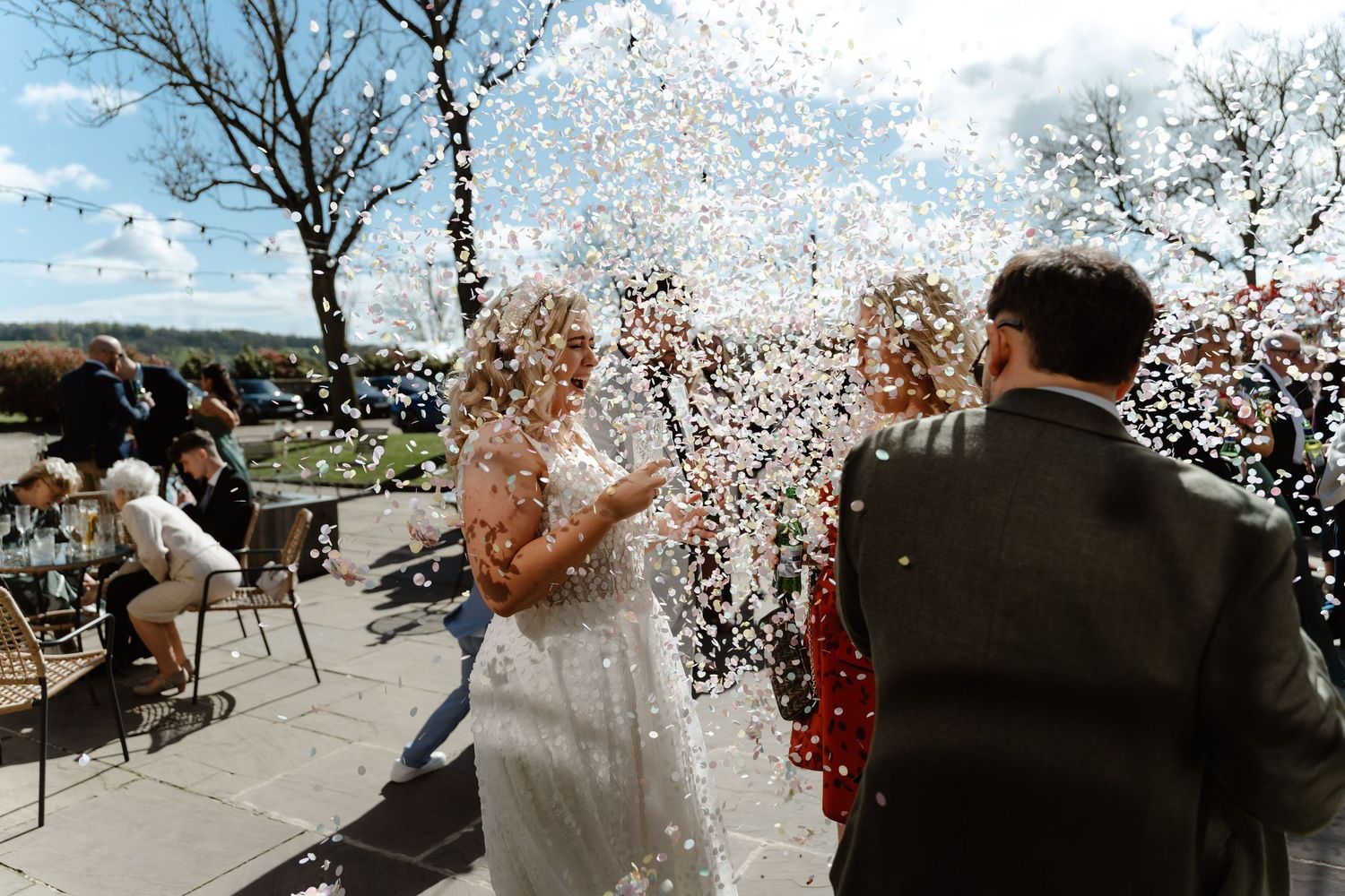 Bride and groom celebrate with confetti shower at outdoor wedding venue on a sunny day.