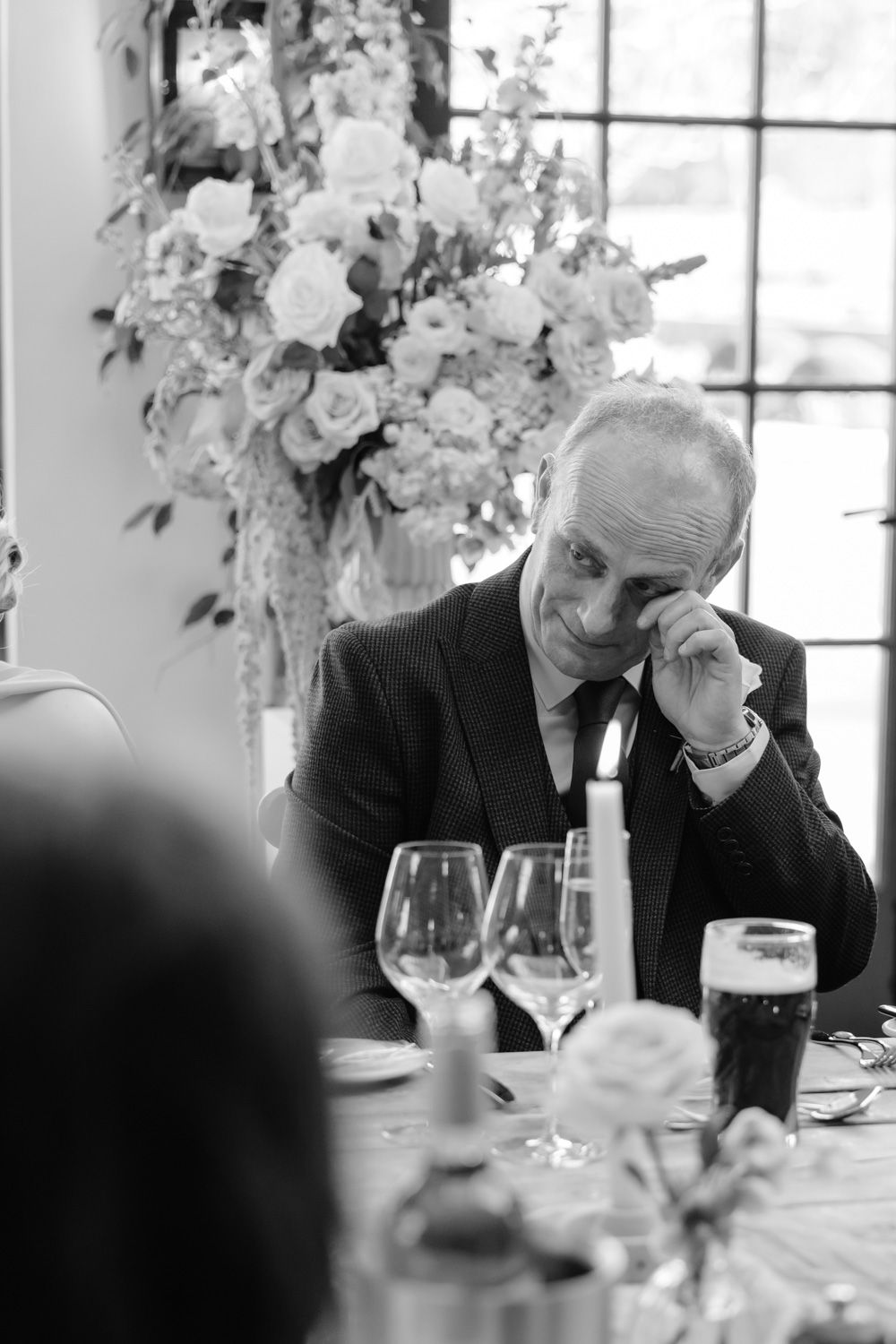 Emotional wedding guest wiping tears at elegant reception table with floral centerpieces.