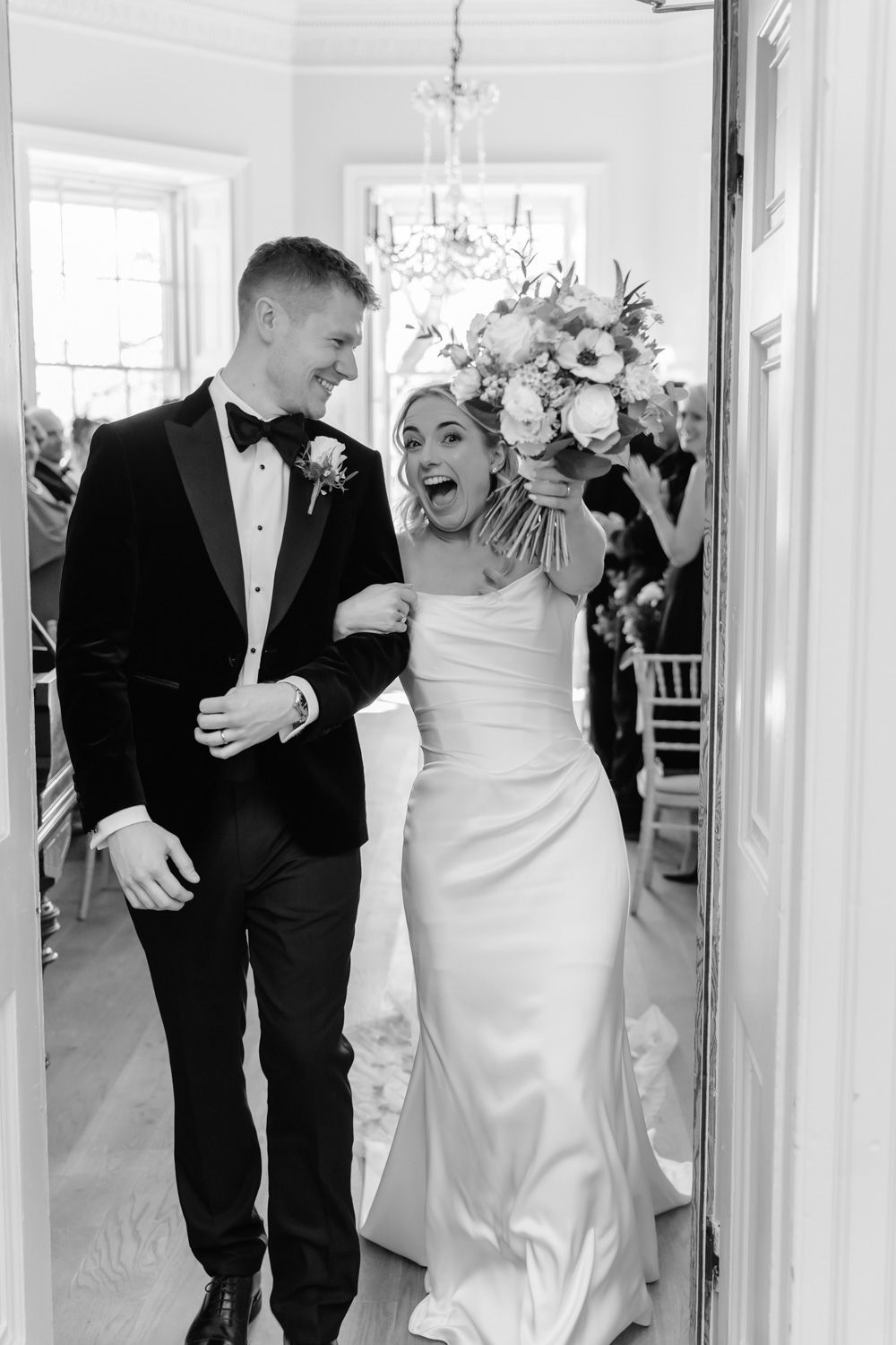 Black and white photo of joyful newlyweds walking back down the aisle after their wedding ceremony.