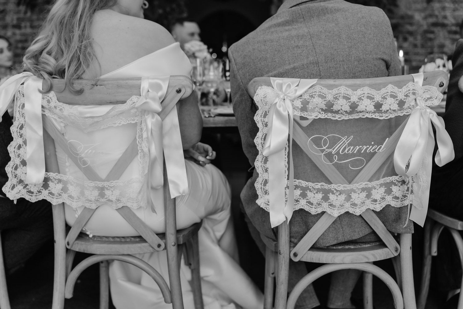 Black and white photo of bride and groom chairs decorated with lace and Just Married signs.