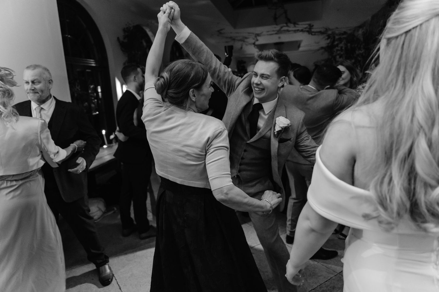 Black and white photo of wedding guests dancing joyfully together on the dance floor at a reception.