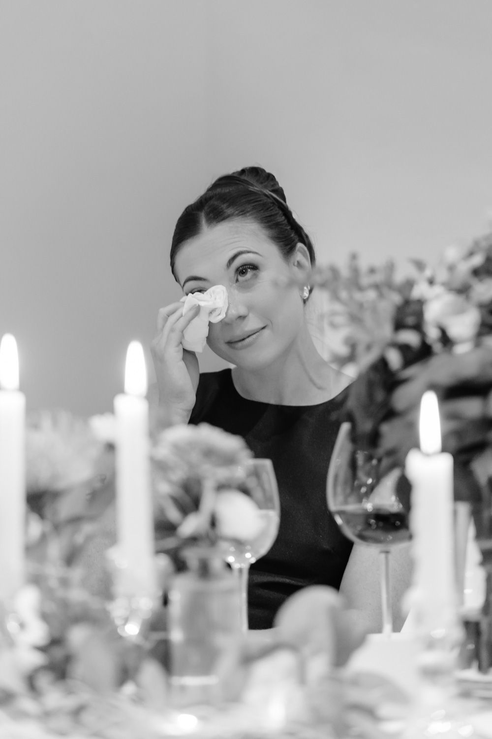 Emotional woman wiping tears at candlelit wedding reception table with flowers.