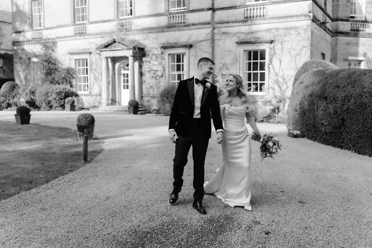 Bride and groom walking happily in front of grand country house estate in black and white.