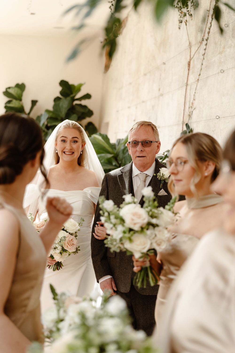 Radiant bride walking down the aisle on her fathers arm surrounded by bridesmaids with bouquets.