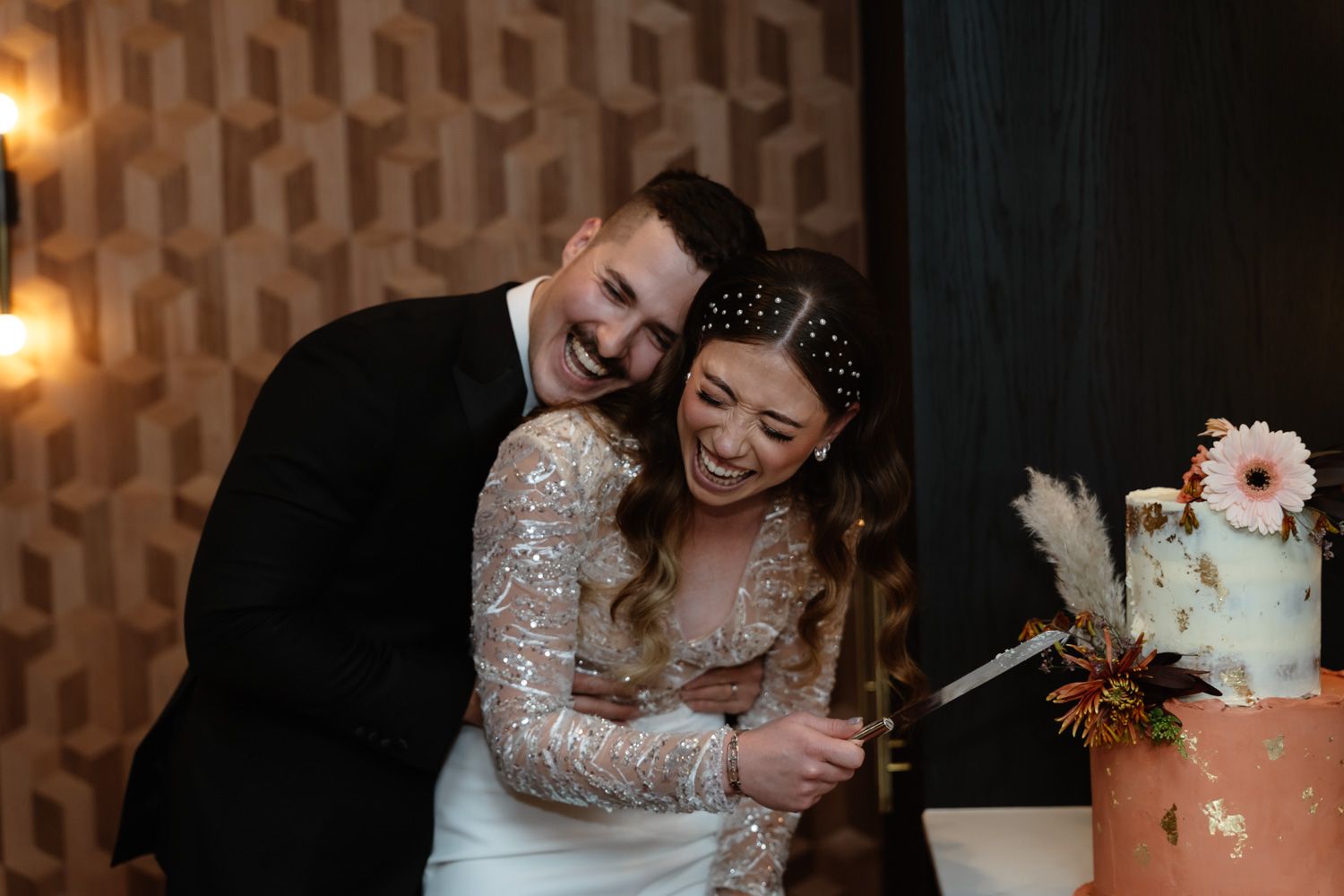 Smiling bride and groom cutting their elegant tiered wedding cake together.